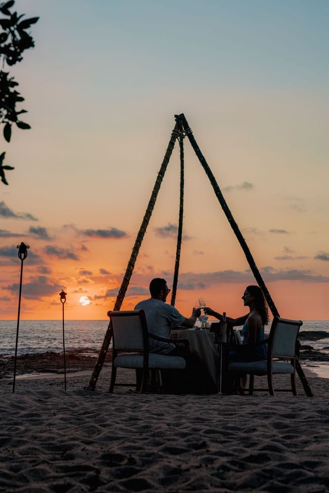 Couple dining under a decorated teepee on a beach at sunset at Cala Luna Boutique Hotel
