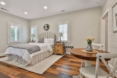 Chic cottage bedroom with plush bed, wooden floor, side table lamps, and a mini dining table by Cottages at Laurel Brooke