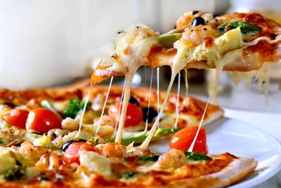 Close-up of a cheesy pizza being lifted, with toppings served in Bistro & Pizzeria at Avaneo Hotel, showcasing hotel images