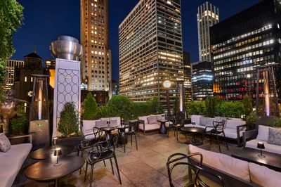 Lounge seating area with white sofas and black tables facing lit skyscrapers at night at The Kimberly Hotel