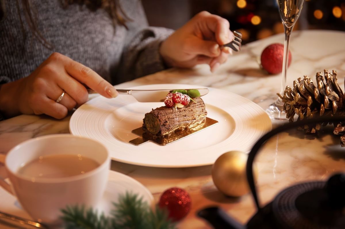 Guest enjoying a festive chocolate log cake, with tea and Christmas decor at The May Fair Hotel