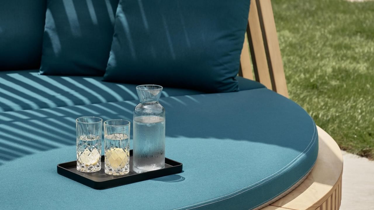 Blue cushioned outdoor seat with pillows, a carafe, and two glasses on a tray at Falkensteiner Luxury Villas