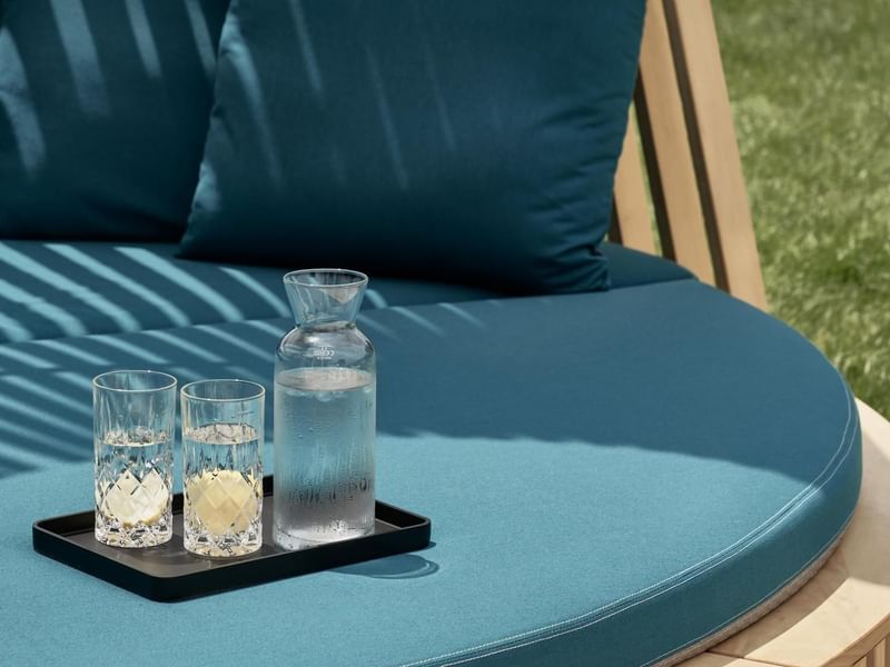 Blue cushioned outdoor seat with pillows, a carafe, and two glasses on a tray at Falkensteiner Luxury Villas