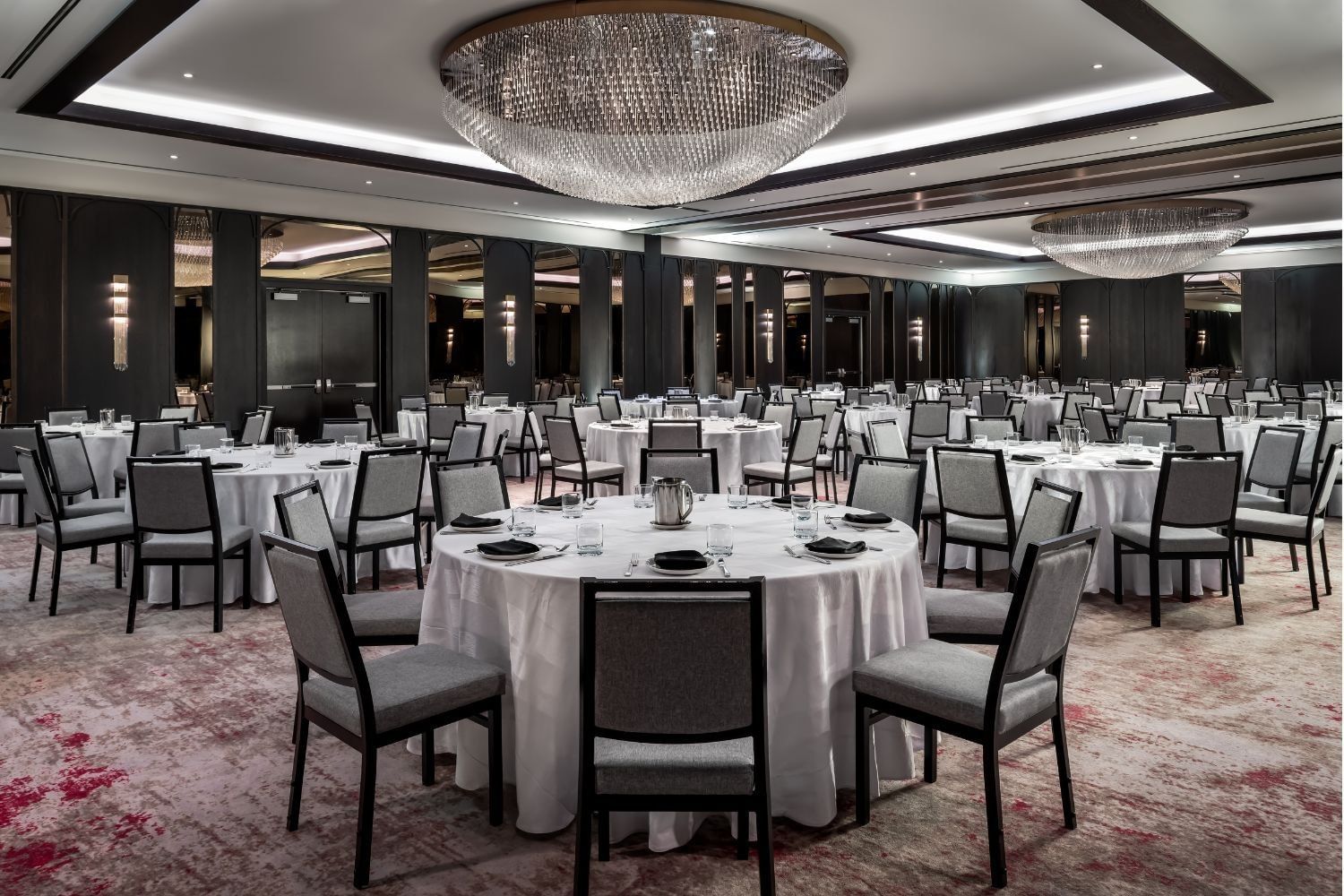 Princes\' Gates Ballroom with round white-clothed tables & grey chairs beneath sparkling chandeliers at Hotel X Toronto