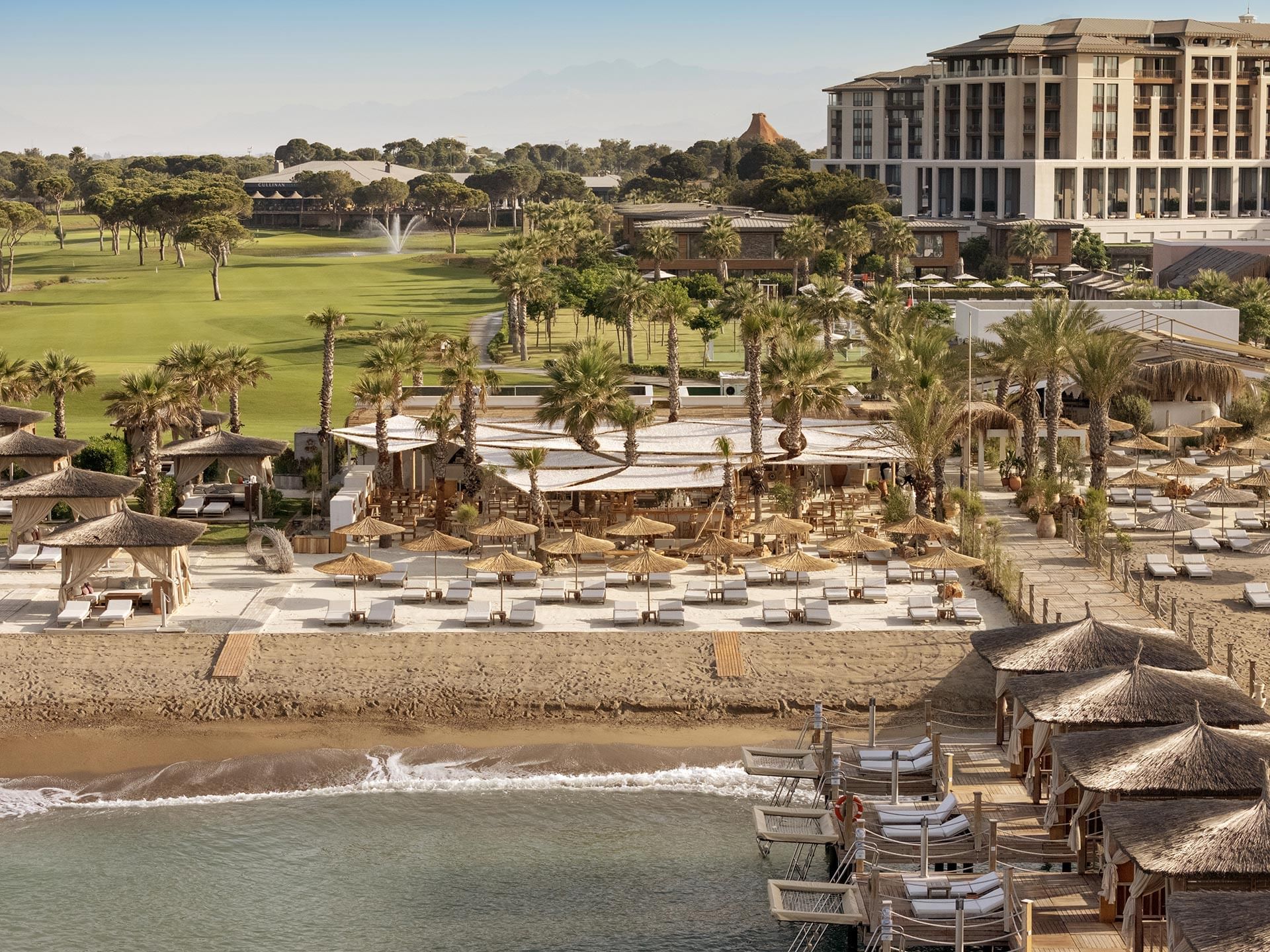 Aerial view of a luxurious resort with beachfront cabanas, palm trees, and a golf course Cullinan Belek.