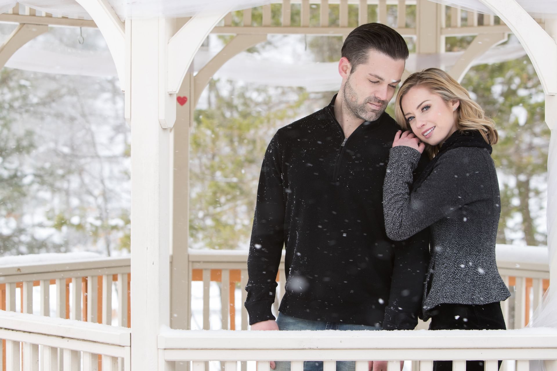 A couple embraces under a gazebo surrounded by falling snow at Cove Pocono Resorts