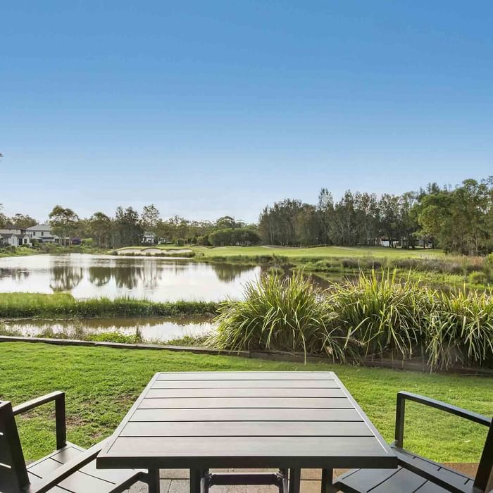 Patio view with a table and chairs overlooking a serene pond and green landscape at Mercure Kooindah Waters