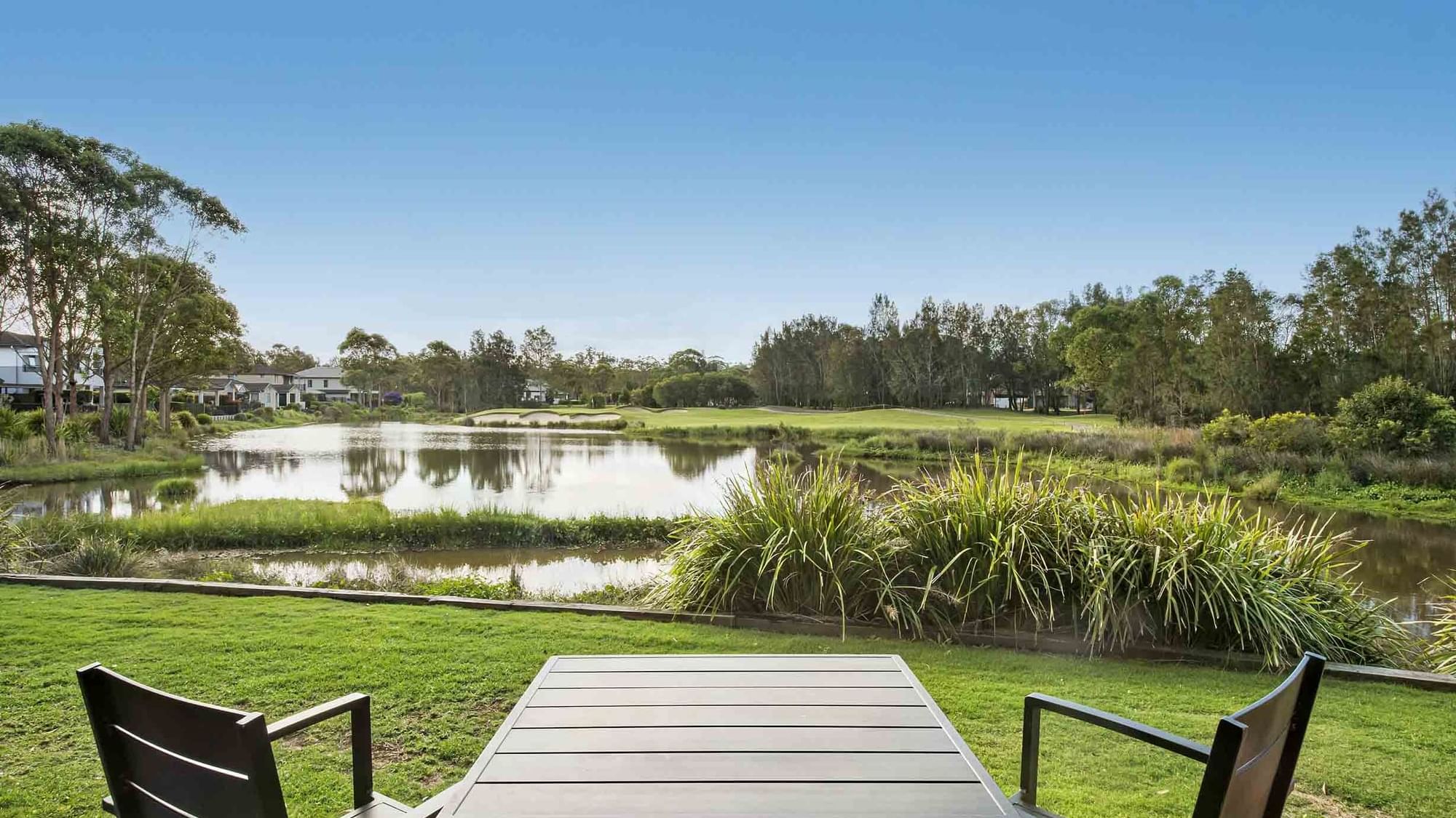 Patio view with a table and chairs overlooking a serene pond and green landscape at Mercure Kooindah Waters