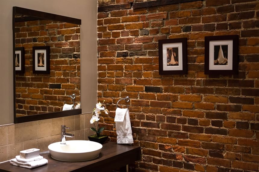 bathroom with mirror and raised sink with exposed brink and artw