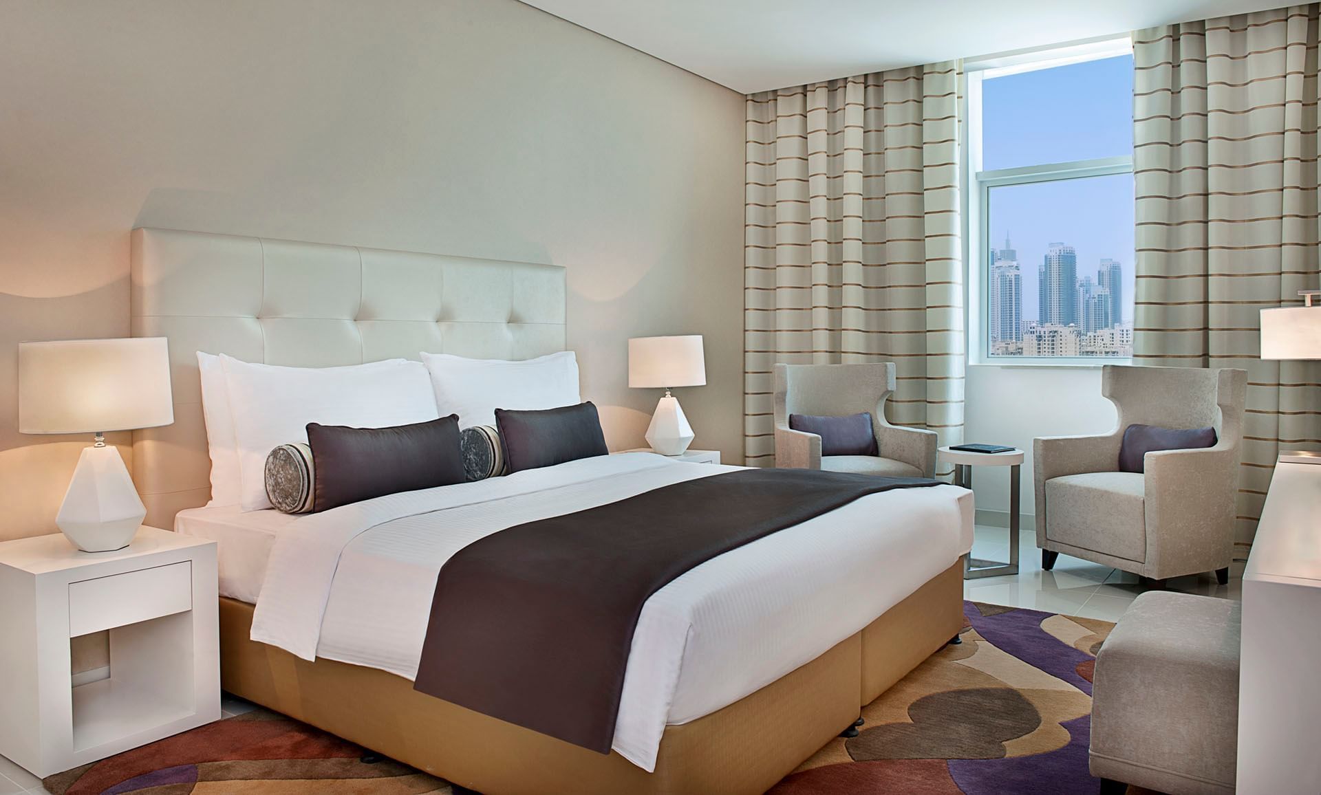 Maison Jardin, Three Bedroom Suite with large bed, two armchairs, lamps, and city view at DAMAC Maison Cour Jardin
