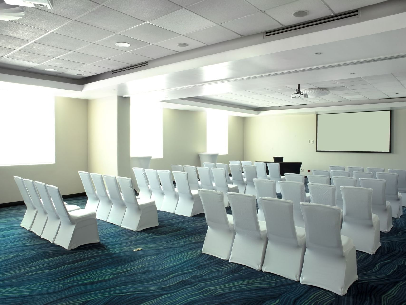 Blue Room with rows of chairs, projector screen and presentation table for event space in San Jose Costa Rica at D Sabana Hotel