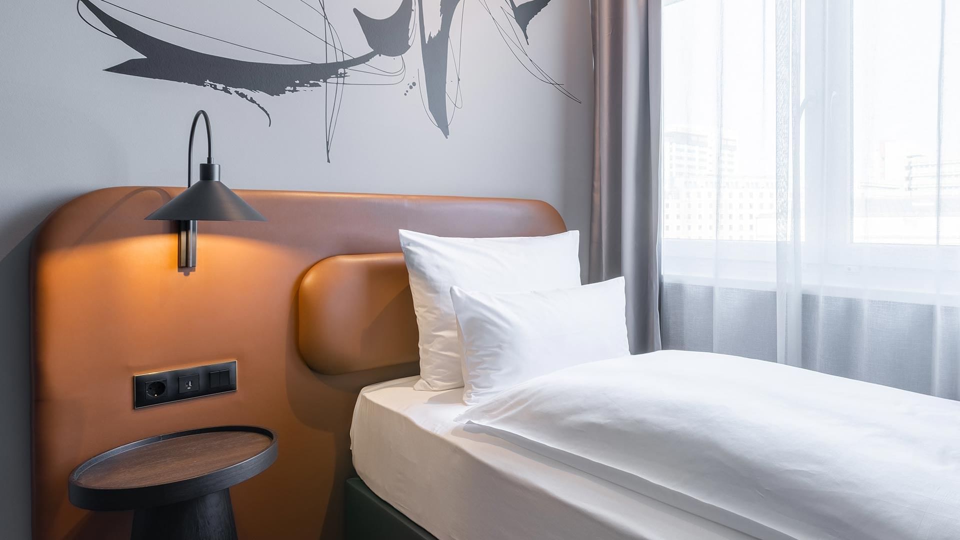 Ein Einzelbett mit Nachttisch im Classic-Einzelzimmer des Titanic Comfort Kurfürstendamm.