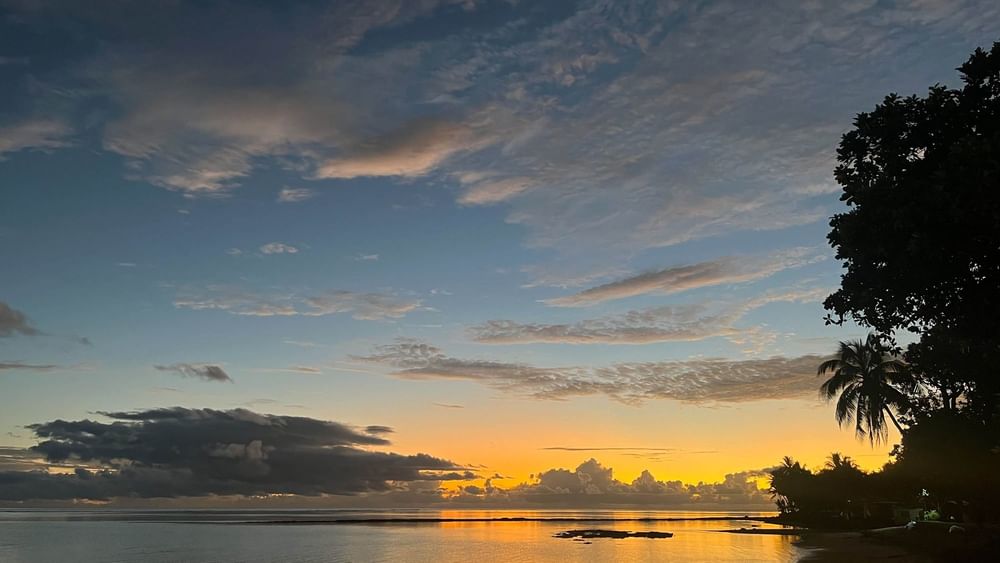 Sunset over calm ocean water with lush trees at The Naviti Resort in Korolevu.