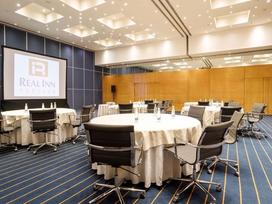 Buenos Aires banquet hall with round tables, white linens, blue striped carpet, and bright lights at Real Inn Torreon