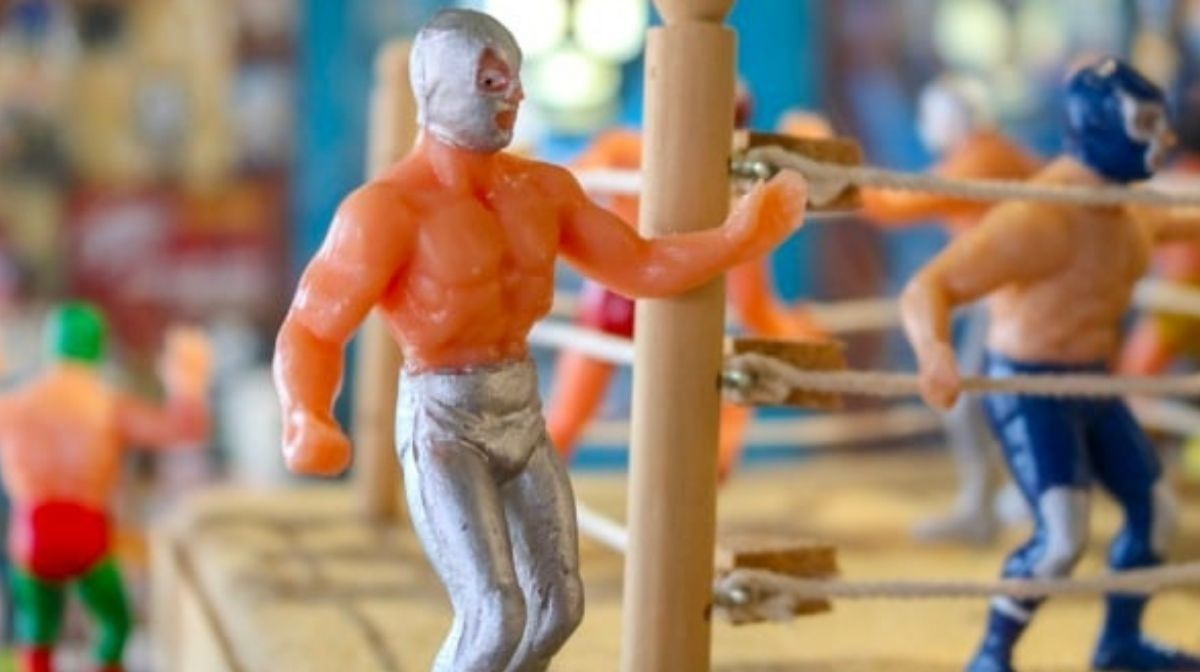 Toy wrestlers by a wooden post under soft light on a ring surface at the Camino Real Pedregal Mexico
