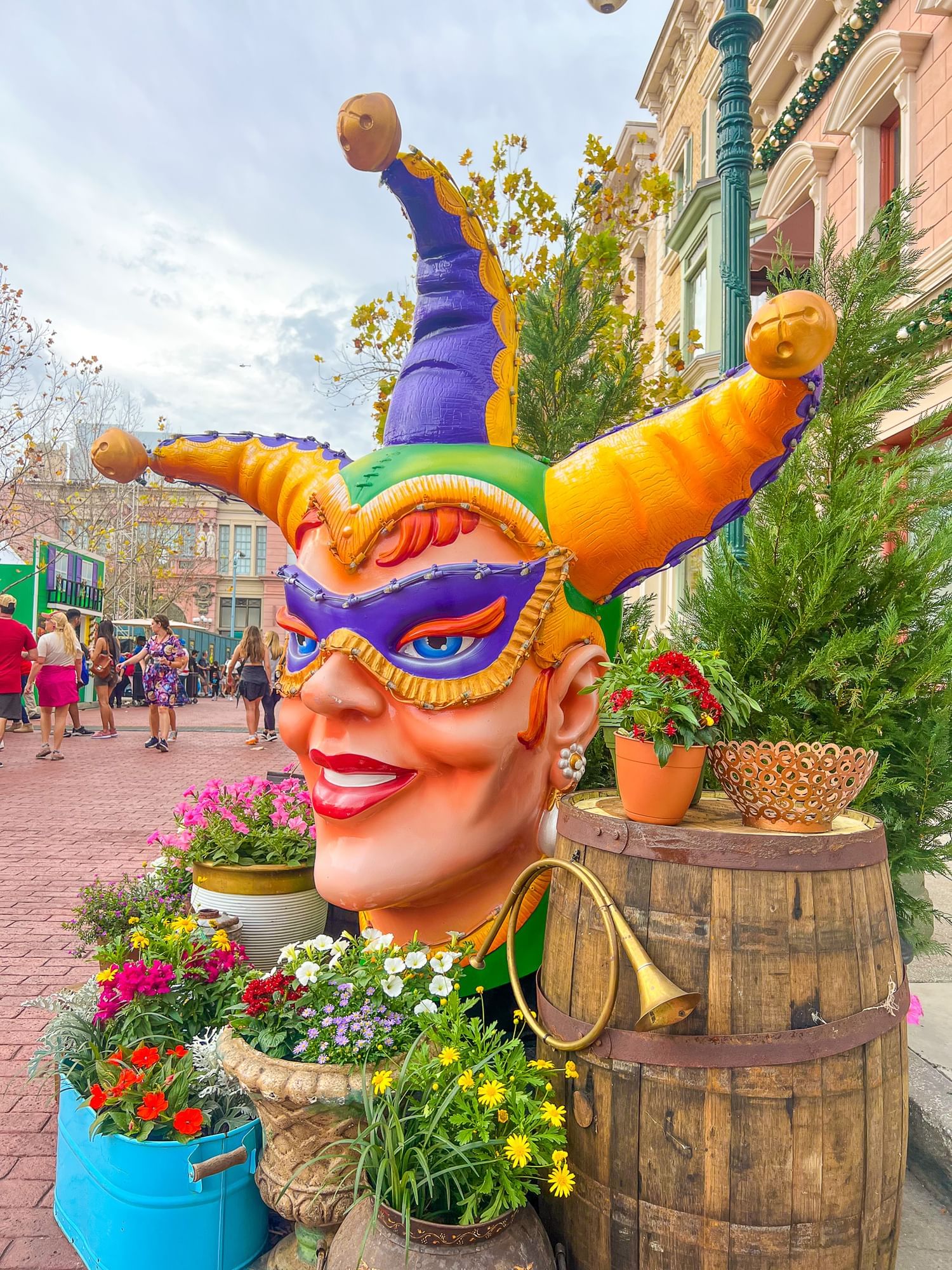 A large, colorful Mardi Gras jester head sculpture at Universal Studios Florida. The jester has a green, purple, and gold hat, a purple eye mask, and a wide smile. 