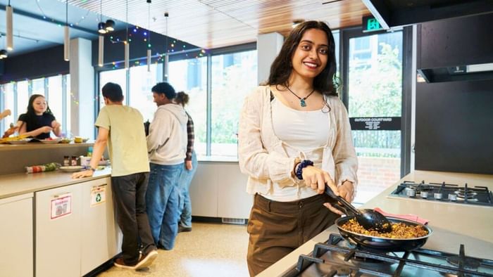 Woman cooking with tongs in the kitchen at UniLodge Royal Melbourne in North Melbourne.