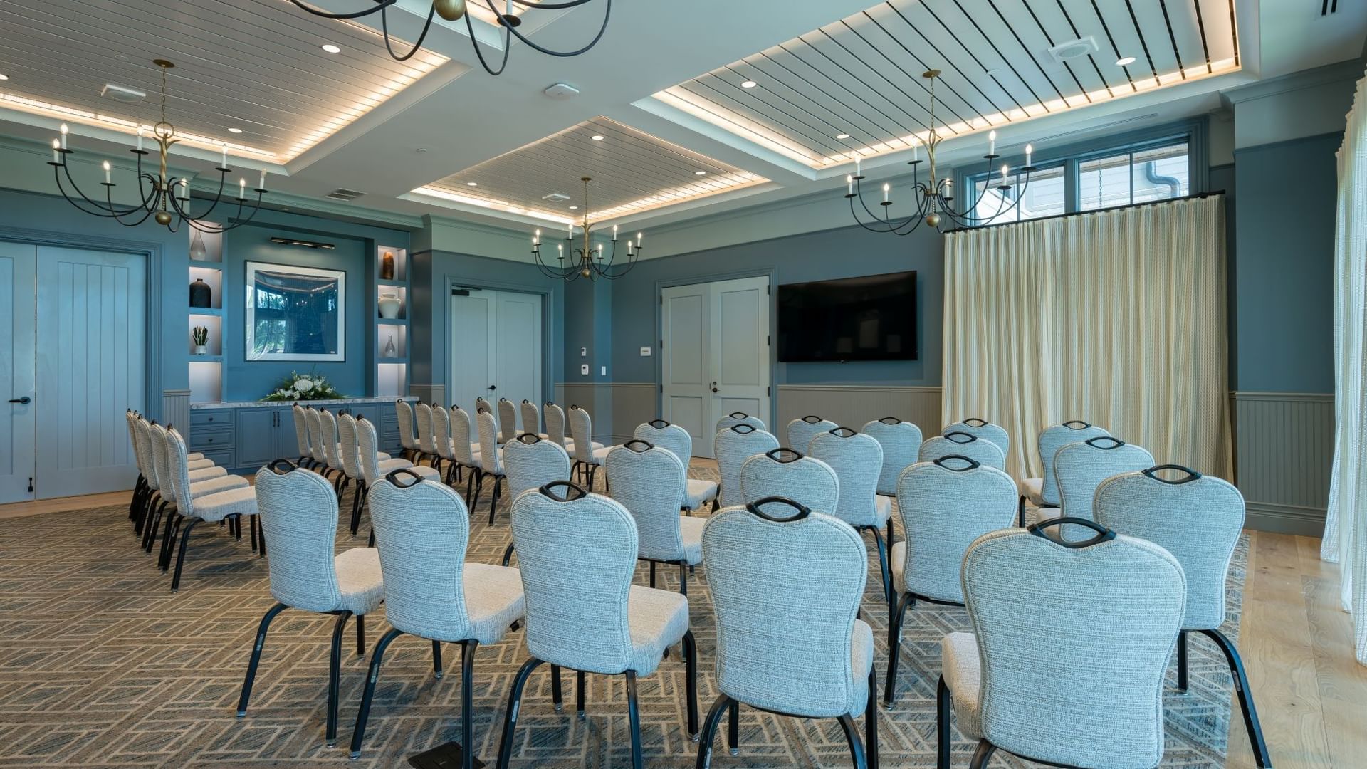Club Room with rows of light blue chairs, decorative ceiling, chandeliers, and large screen at Camp Creek Inn, Inlet Beach.