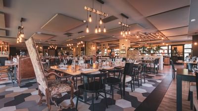 A restaurant with hexagonal tile floor, wooden tables, black chairs, and hanging lights on the ceiling.
