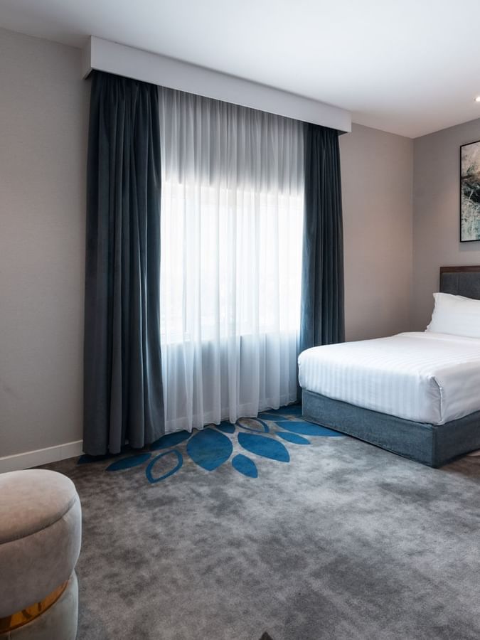 Two beds in Family Suite Sea View by a wooden desk with a flower vase and grey stool at Warwick Al Jubail