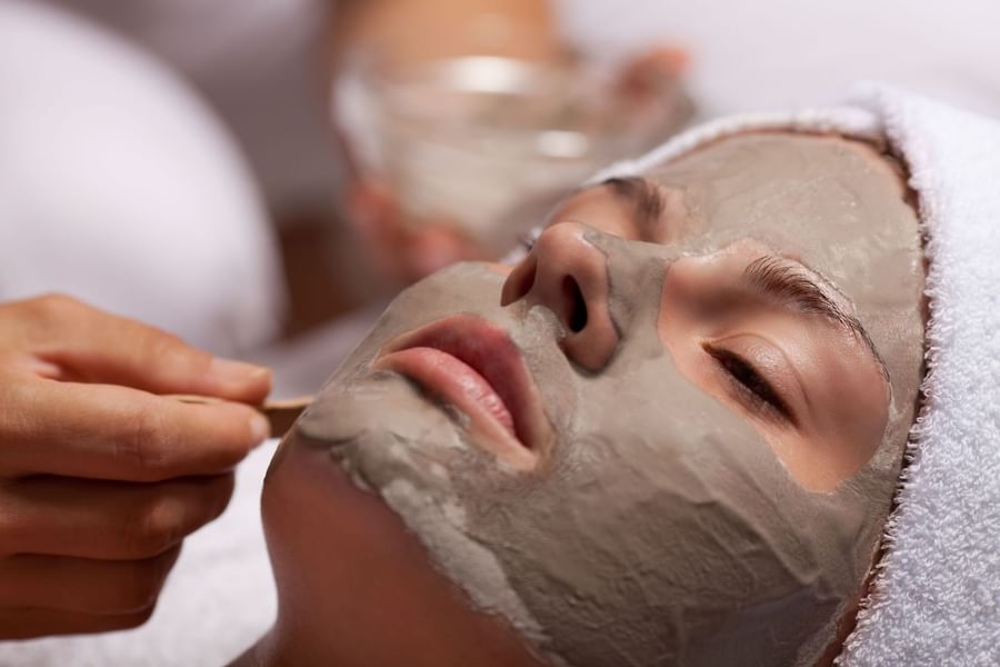 A woman relaxes as a gray clay face mask is gently spread with a spatula at May Fair Spa, The May Fair Hotel
