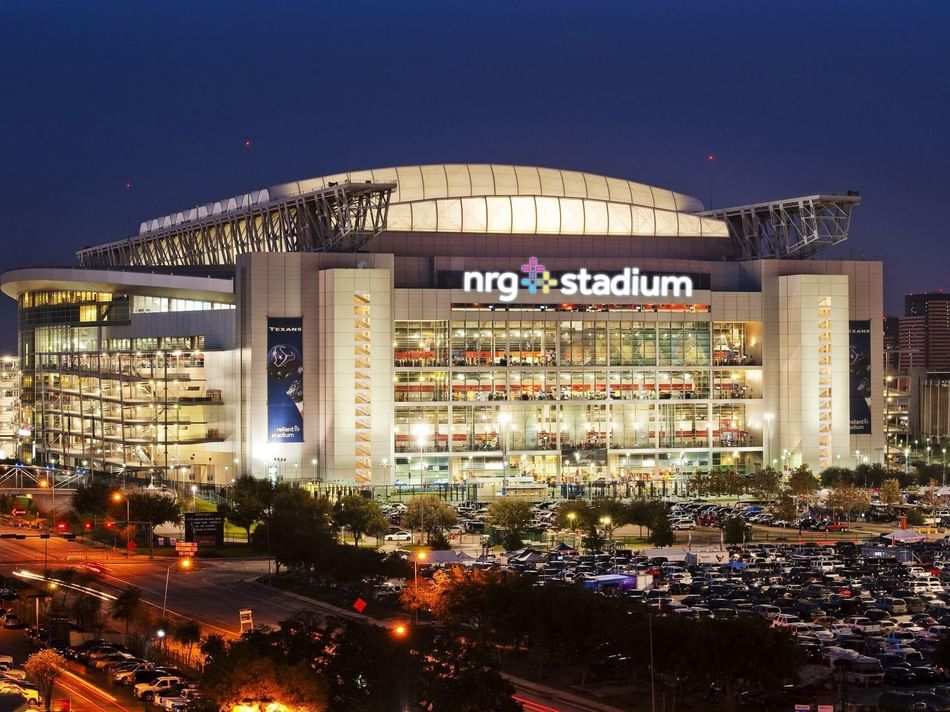 NRG Stadium near Granduca Houston, lit up at night with modern architecture and a busy parking area