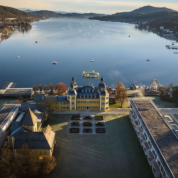 Zračna slika dvorca i uređenog vrta uz jezero s brodicama i zabavnim parkom.