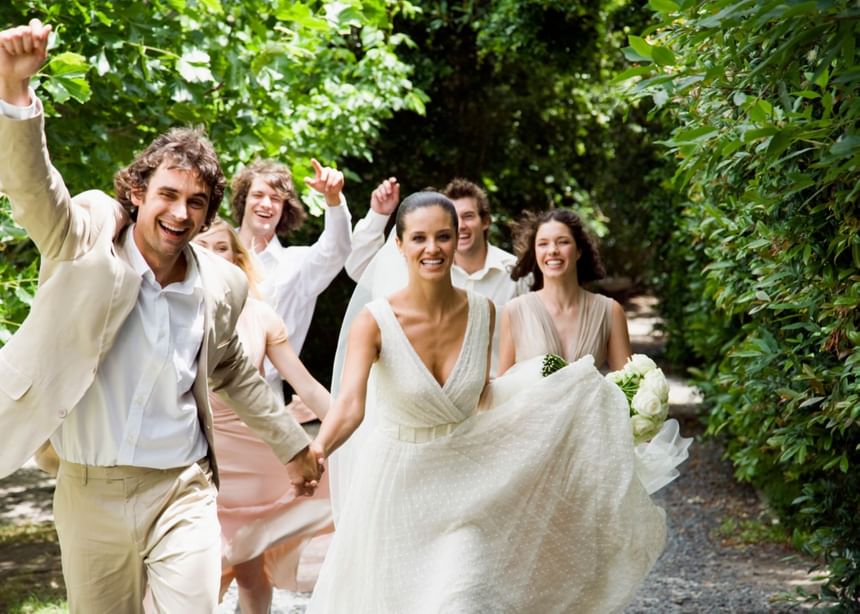 Bride and groom, accompanied by their wedding party, walking down a path at The Bethel Resort & Suites