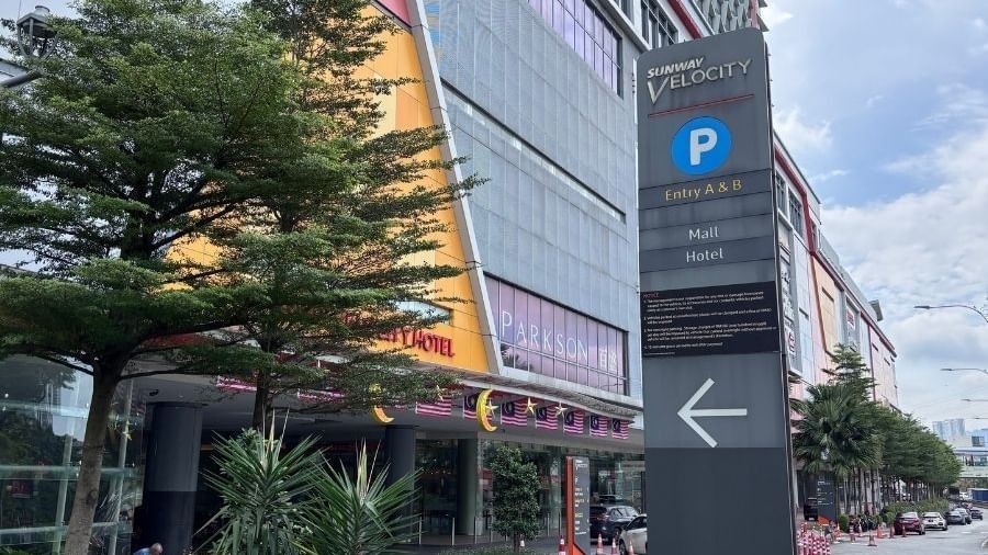 Sign for Sunway Velocity parking entrance with arrow pointing right, next to a building and trees.