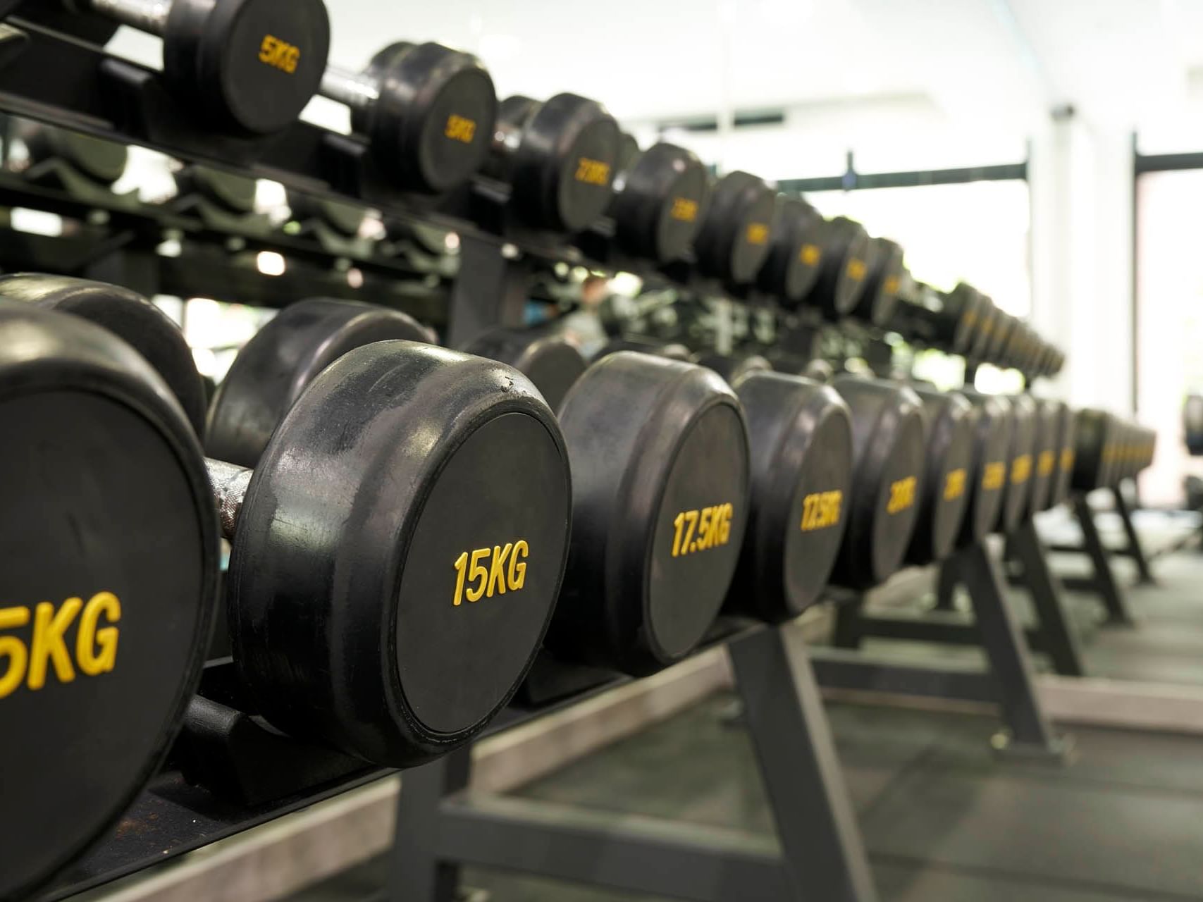 A neat row of black kilogram-labelled dumbbells on a rack in the modern gym at Orchard Grand Court