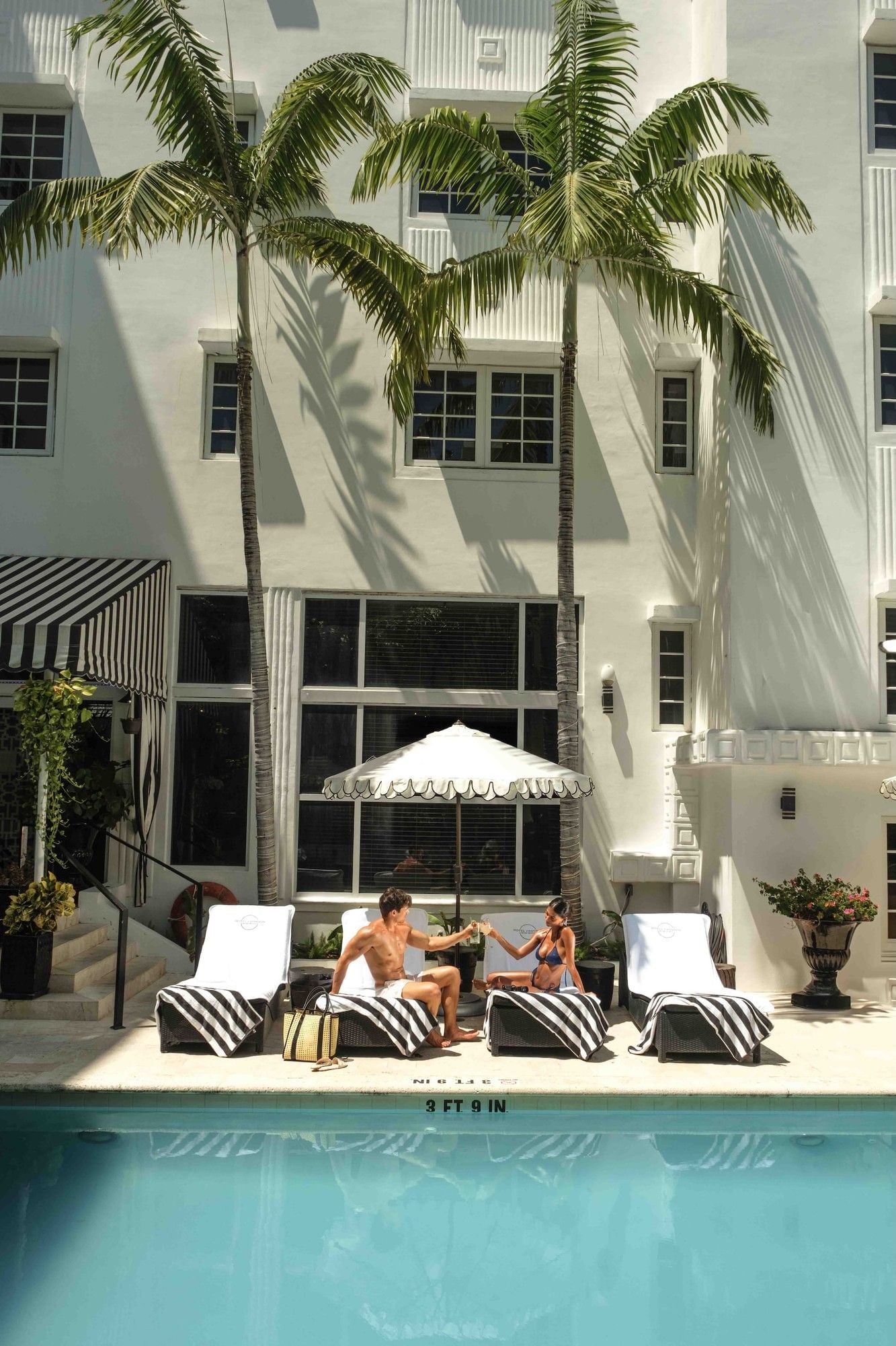 A couple relaxes by the pool in front of a white building.