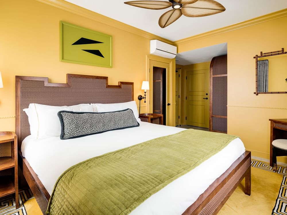 A wide view of a hotel room with a king-sized bed, yellow walls, and a ceiling fan.