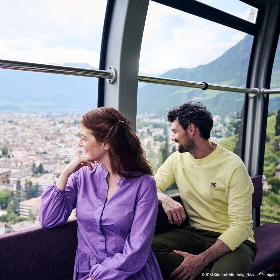 A couple is sitting on a cable car, enjoying a view of a city below.