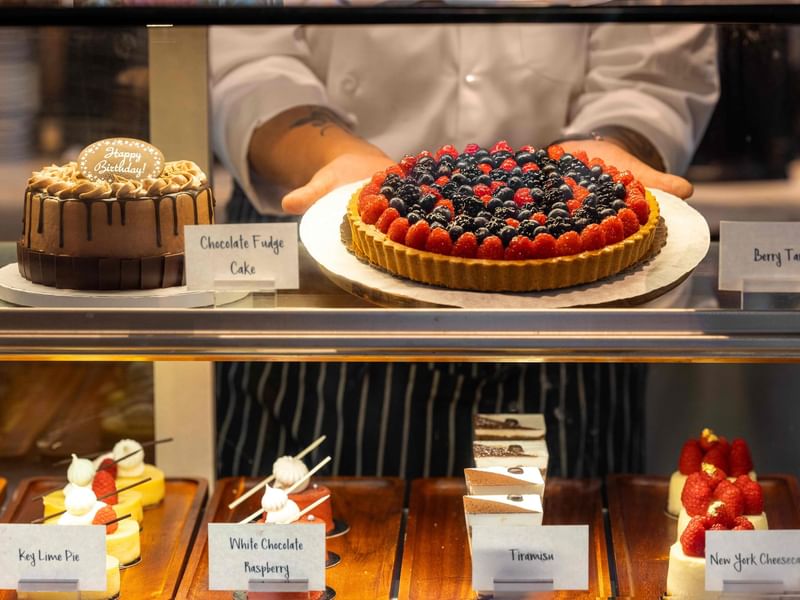 The Press pastry chef showcases chocolate fudge cake and berry tart in a glass case at The Diplomat Resort