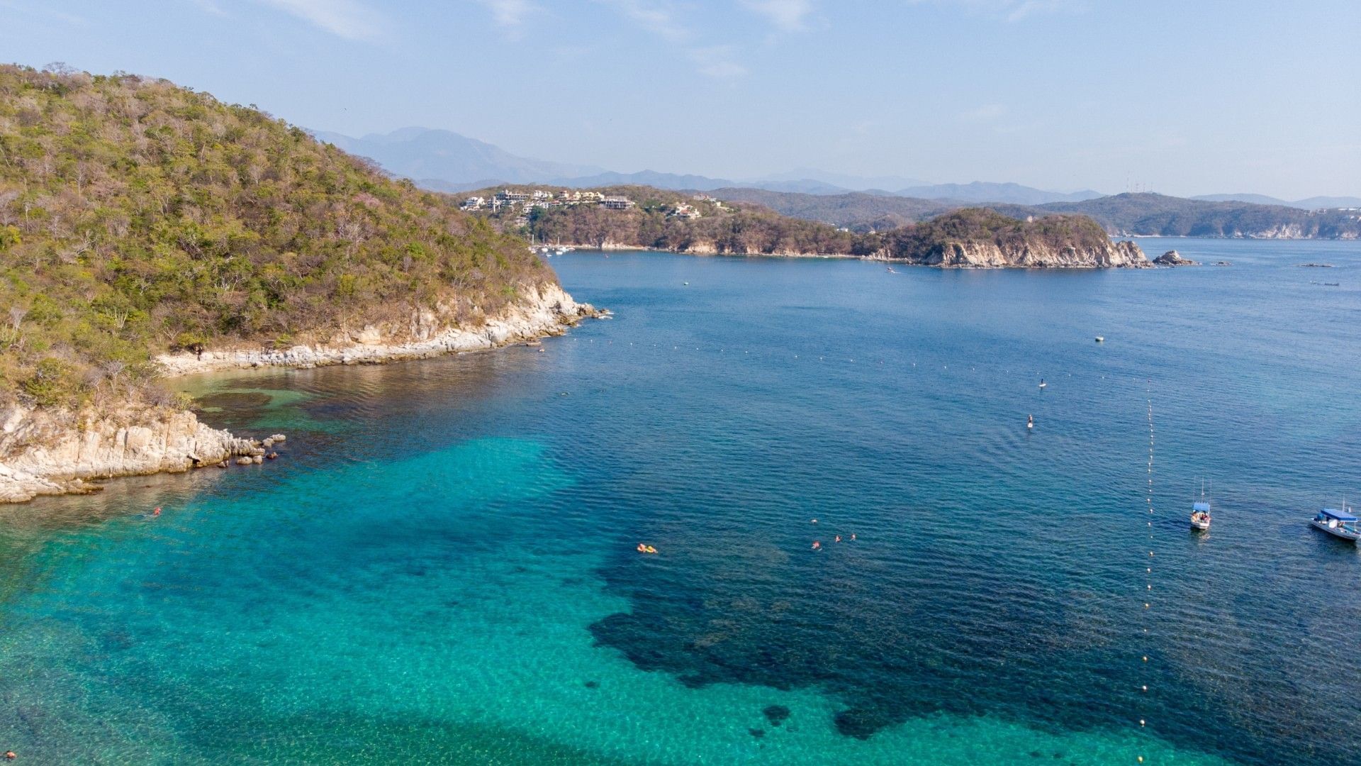 Aerial view of turquoise ocean bays by rugged cliffs under a clear blue sky near Quinta Real Huatulco