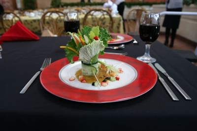 Fresh garden salad appetizer on a red-rimmed plate by wine glasses and a red napkin at Glenmore Inn & Convention Centre