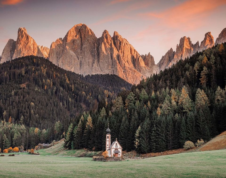 Small St John Church in Ranui nestled in green valley below dramatic Dolomite mountain peaks view near Meraviglia