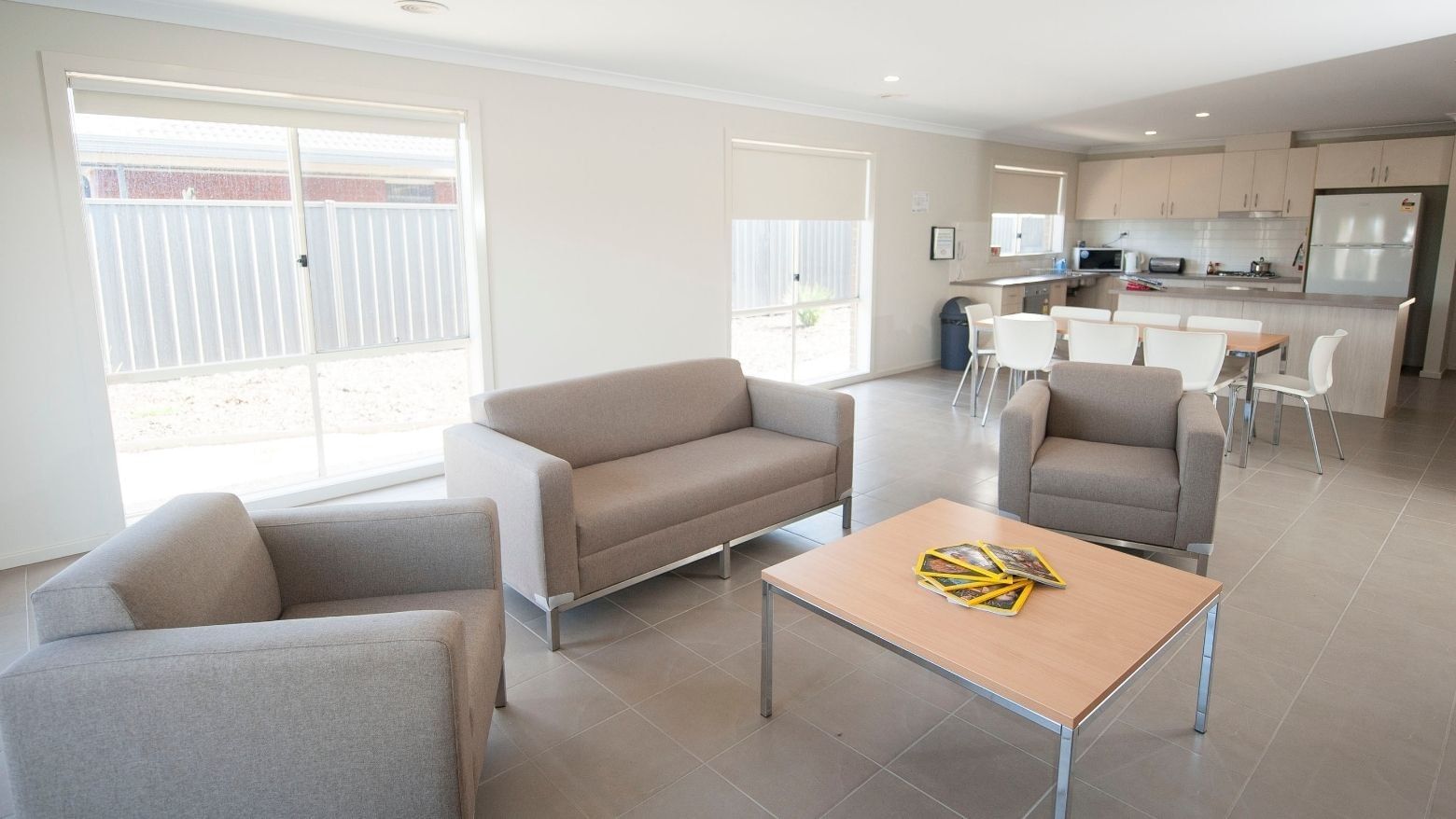 Three gray armchairs, a wooden coffee table, and an open kitchen area in La Trobe University Regional Housing – Shepparton.