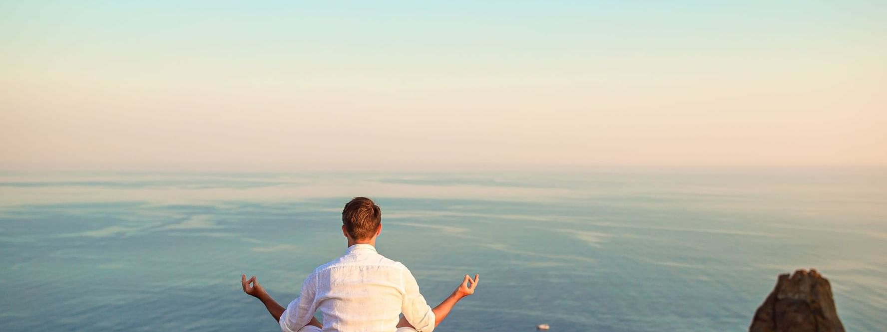 Man meditating peacefully on a cliff overlooking the vast ocean, near the Marquis Los Cabos Resort
