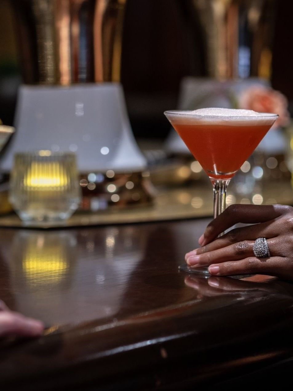 Guest holding a red cocktail by a martini glass on a dark wooden bar counter in Margaux Lounge Bar at Warwick Seattle