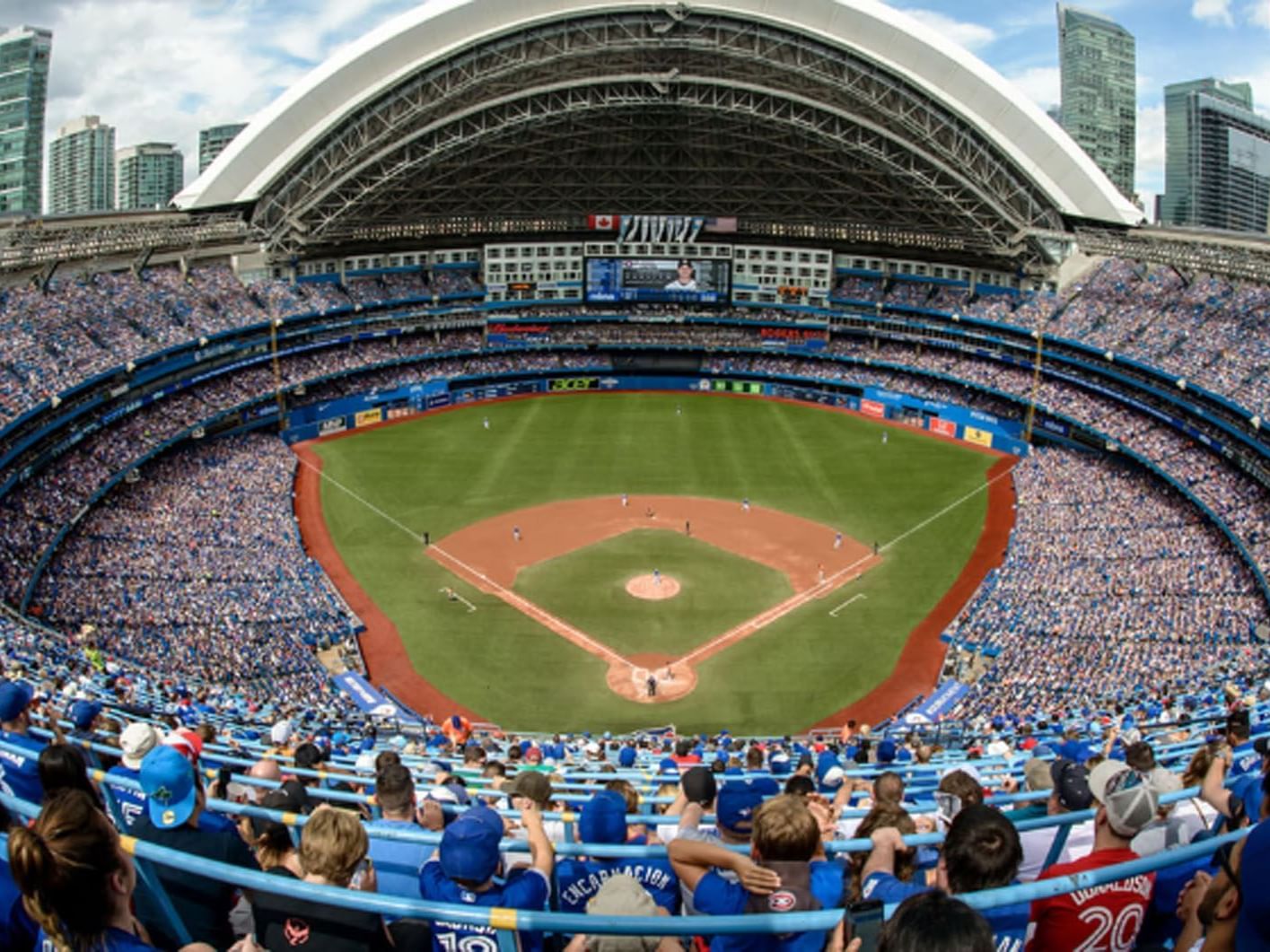 Rogers Centre with fans in blue jerseys watching a game, with an open retractable roof near Hotel X Toronto