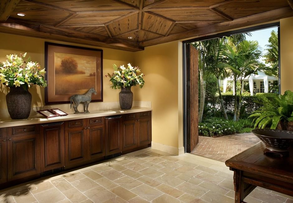 Wooden counter with flower vases under a framed picture beside open doorway looking at the palm garden at The Brazilian Court