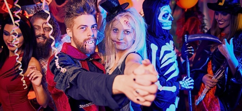 Group of people in Halloween costumes dancing and celebrating at a party.