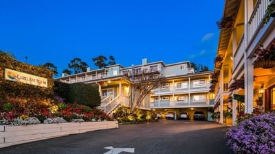 Beautifully lit hotel exterior and sign at dusk surrounded by colorful flowers and lush landscaping at Carmel Bay View Inn