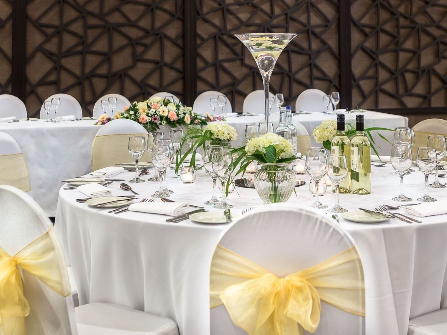 Banquet setup featuring white tables adorned with crystal glassware, floral centerpieces, and wine at Heston Hyde Hotel