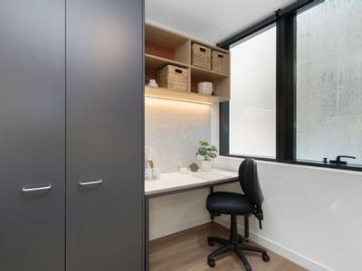 Tidy desk with chair, plant, window, gray wardrobe, and open shelving with baskets.