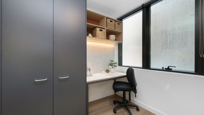 Tidy desk with chair, plant, window, gray wardrobe, and open shelving with baskets.