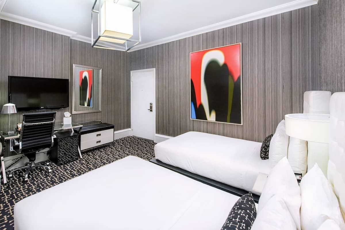 A wide view of a hotel room with two beds, a TV, desk, and artwork
