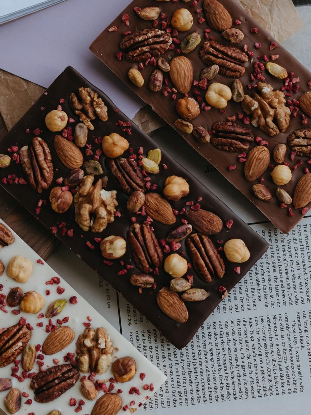 Three chocolate bars with nuts and berries on a newspaper, showcasing Belgian Flavours Escape.