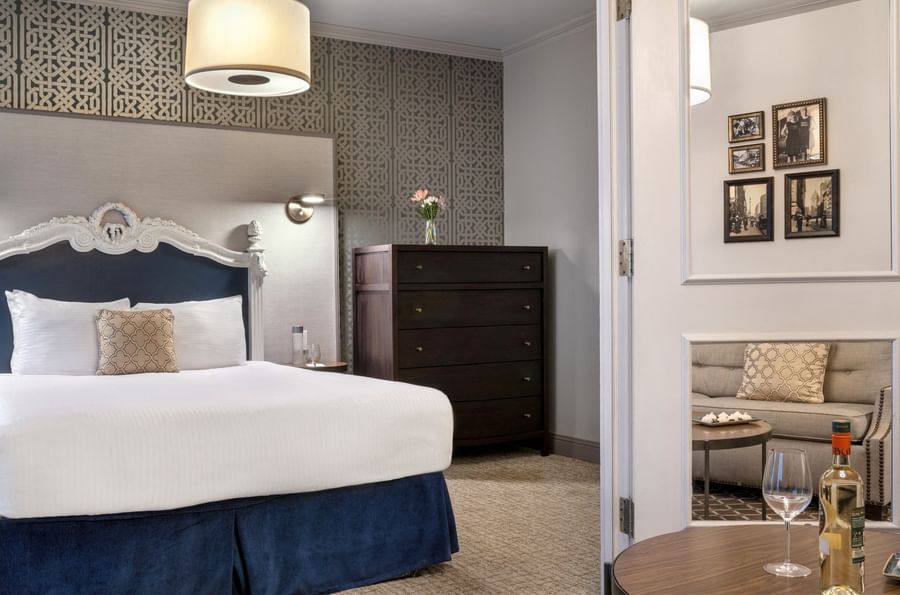 Dark wood dresser by a bed under a drum lamp near a white-framed doorway in Grand Suite at Warwick San Francisco